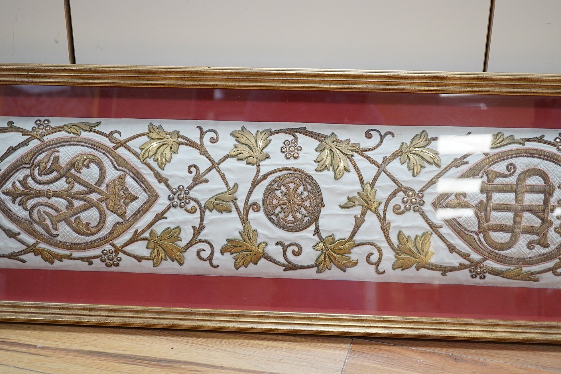 A framed Continental late 18th / 19th century heavily embroidered and deeply couched gold thread and white silk Orphrey panel, possibly part of a Chasuble or similar ecclesiastical garment, 18cm wide x 124cm long. Condit